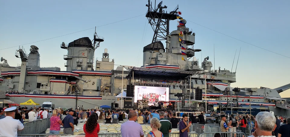 The outdoor display with attendees gathered in front of the battleship.