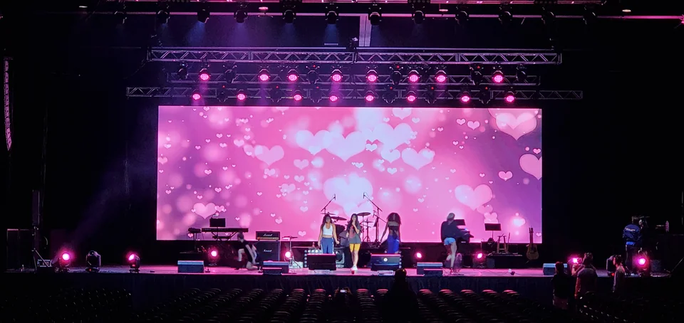 Pink stage visuals behind performers with seating in the foreground.